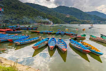 Colorful wooden boats floating on the calm waters of Phewa Lake in Pokhara, Nepal, surrounded by lush green hills and the dramatic Himalayan landscape of the Annapurna region © Yuliia