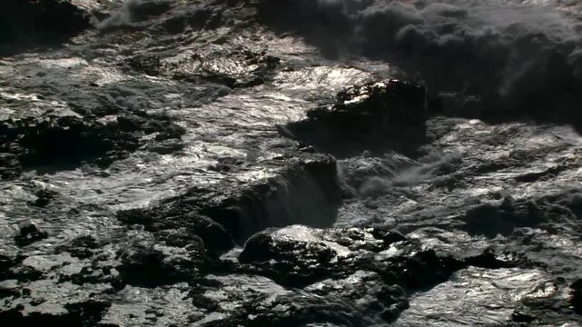 Turbulent ocean water churning with white foam and dynamic wave motion over dark rocky shoreline