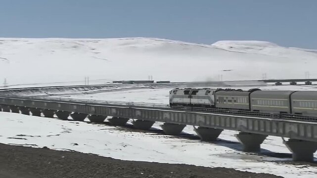 Diesel locomotive pulling passenger train across elevated railway bridge in snow-covered high-altitude plateau landscape