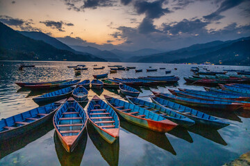 Colorful wooden boats floating on the calm waters of Phewa Lake in Pokhara, Nepal, surrounded by lush green hills and the dramatic Himalayan landscape of the Annapurna region © Yuliia