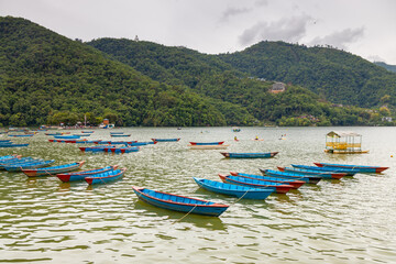 Colorful wooden boats floating on the calm waters of Phewa Lake in Pokhara, Nepal, surrounded by lush green hills and the dramatic Himalayan landscape of the Annapurna region © Yuliia