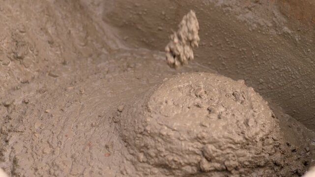Close-up view of wet concrete slurry with uneven lumps, rounded buildup, and glossy moist patches covering rough coated surface.