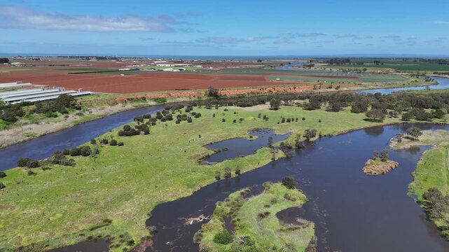 Aerial drone view of Werribee River at Werribee South, Melbourne, Victoria, Australia, with the river splitting around islands and grassy floodplain flats, eroded bank and ploughed farmland beyond