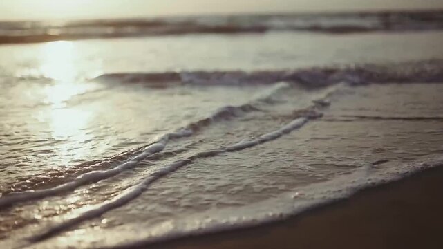 Close-up of gentle ocean waves washing ashore on golden-hour beach with foamy white edges and sunlit water surface