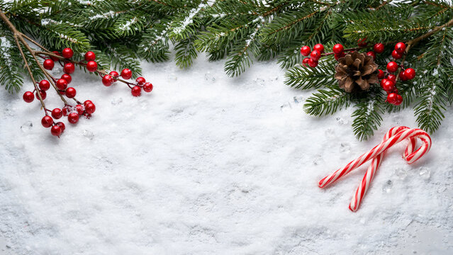 Christmas background with fir branches, red berries, pine cone and candy canes on snow