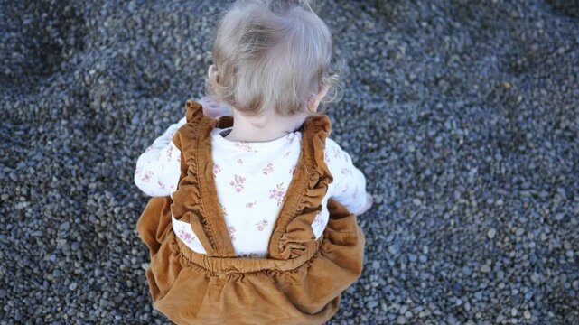: Infant Girl Plays with Rocks in Playground