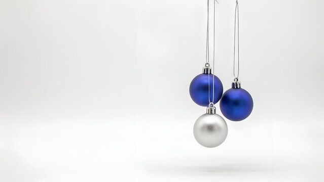 Two blue and one silver christmas ornaments hanging against a clean white background