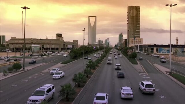 Aerial drone view of Riyadh&rsquo;s King Fahd Road with the Kingdom Tower and Kingdom Centre skyline at golden hour, featuring flowing traffic and urban infrastructure