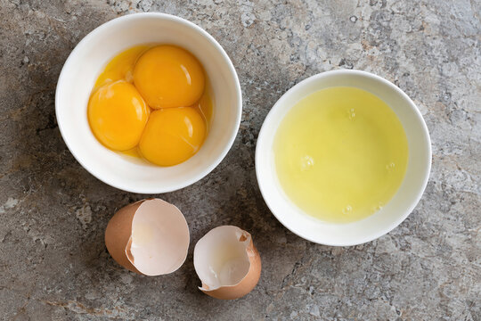 Raw egg yolks and whites separated into two bowls