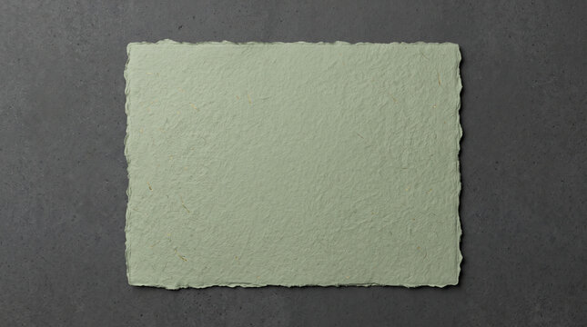 Pale green handmade paper sheet with deckle edges on a dark grey stone background for a sustainable product mockup stage presentation