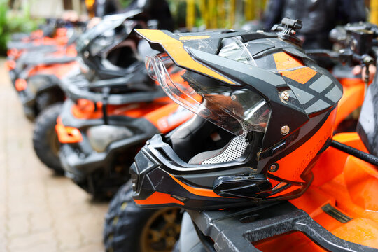 Off road helmet in orange and black displayed on all terrain vehicle at outdoor powersport dealership with rugged gear and vehicles nearby