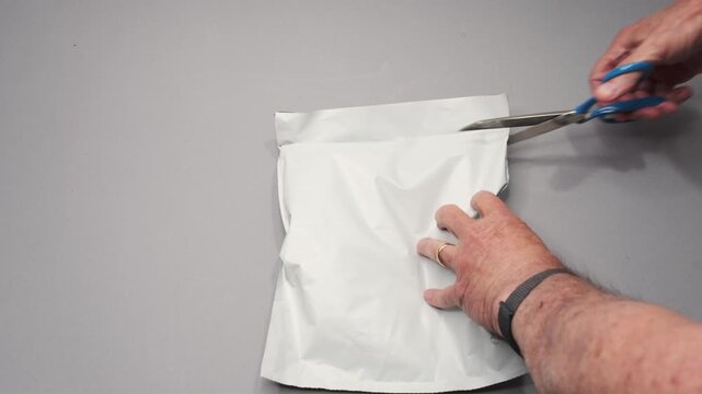 An older man is cutting open a mailer envelope to retrieve a prescription inside.