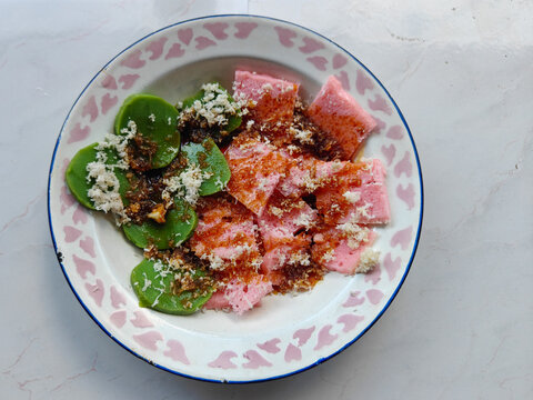 Traditional Indonesian kue putu ayu and apem cake served with grated coconut and liquid palm sugar on a plate