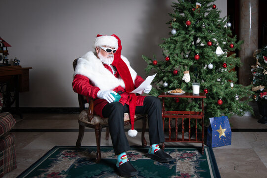 Santa writing naughty and nice list beside Christmas tree