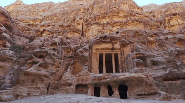 Handheld panning view, ancient Nabataean rock cut facade at Siq al-Barid, surrounded by weathered sandstone cliffs and carved chambers