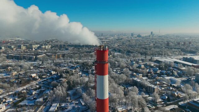 Red and White Industrial Chimney Emitting Steam Over Snowy Riga Skyline, Latvia