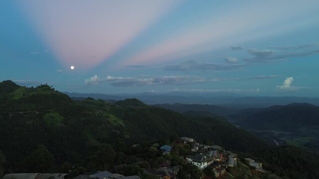 Mountain Village Beneath Colorful Twilight Sky with Glowing Moon, Forested Ridge, Tropical Hills, Distant Valley, Scattered Homes, and Peaceful Landscape Scene