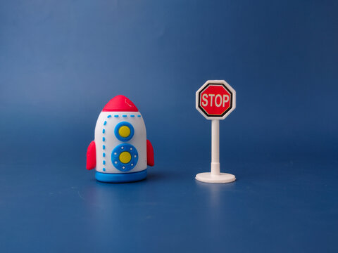 A toy rocket with a red nose cone and blue markings stands next to a miniature stop sign
