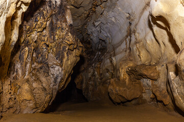Interior of Tham Hoi cave in Laos showing limestone rock formations, textured cave walls with mineral deposits, and a dark passage leading deeper underground. © Eugene Ga