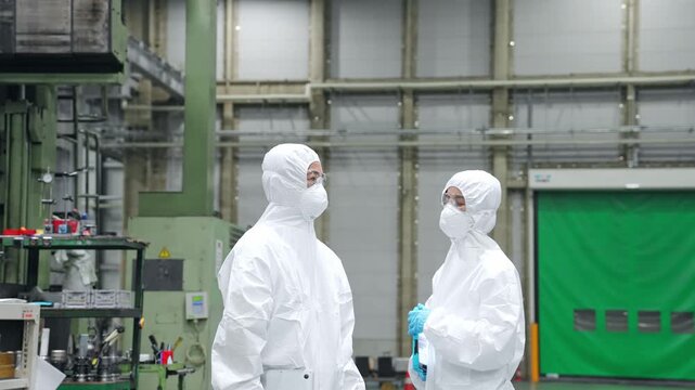 防護服を着て工場の中で話す男女作業員