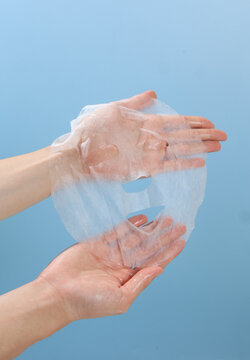 A pair of hands is displaying a sheet mask against a clean, solid-colored background.