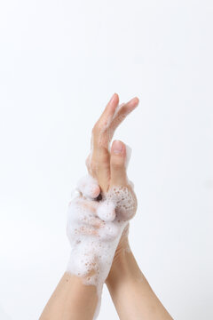 A pair of hands is using soap to create a lather for cleaning, set against a clean, solid-colored background.