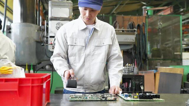 A male factory worker uses a handheld terminal to inspect products.