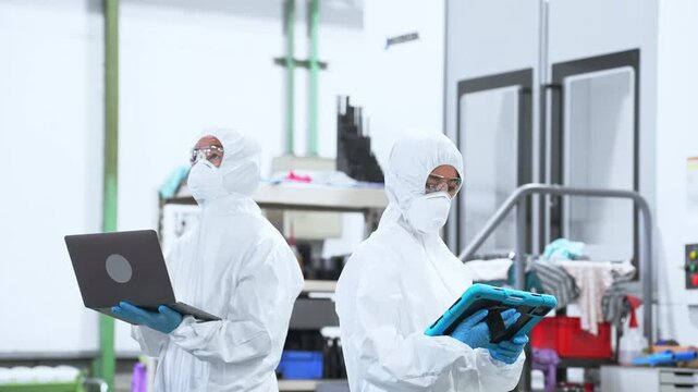 デジタルデバイスを持って工場で作業する防護服を着た男女作業員