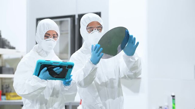 半導体工場でタブレットを持ってシリコンウエハーを検査する防護服を着た男女作業員