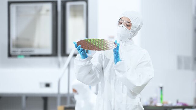 半導体工場でシリコンウエハーを検査する防護服を着た女性作業員