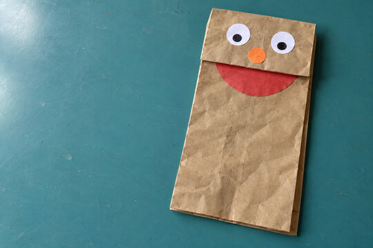 Paper Bag Puppet with Paper Eyes and an Orange Nose on a Teal Table