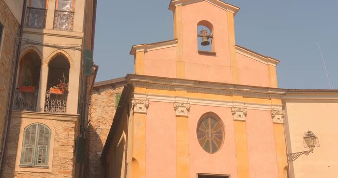 Pastel pink church with bell tower in Apricale, a medieval hilltop village in Liguria.