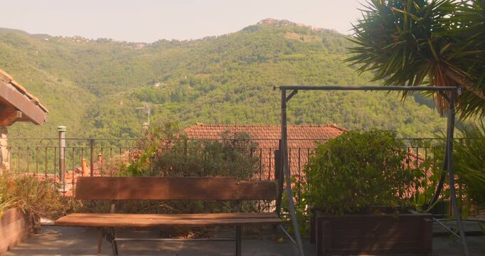 Terrace bench overlooking terracotta rooftops and forested hills in Apricale. Warm golden light.