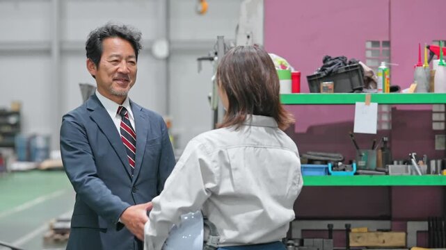 工場で握手する男性ビジネスパーソンと女性作業員