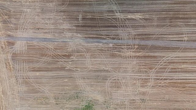Top-down drone view of a harvested agricultural field, with tire tracks, crop stubble, and a farm track crossing brown soil near S&uuml;meg, Hungary, in late summer.