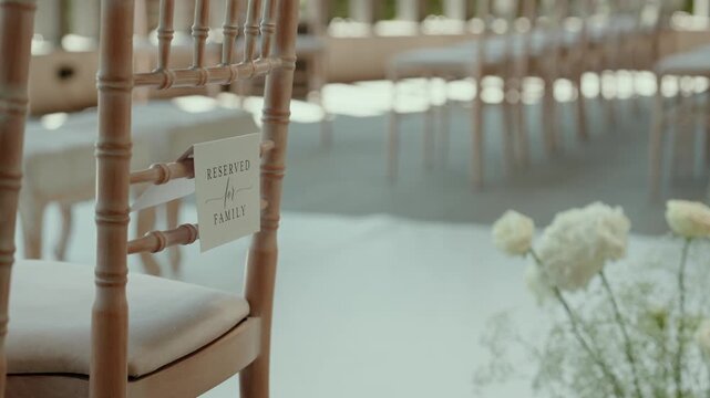 Reserved for Family card hangs on a front row chair beside white aisle flowers, with blurred ceremony seating behind.