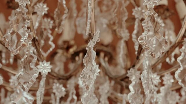 Detail of cut crystal pendants and star shaped rosettes hanging from a gilded antique chandelier arm.