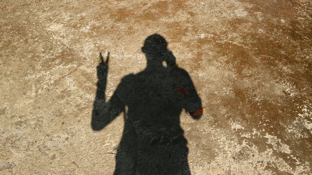 Shadow of a person making peace sign on dusty ground