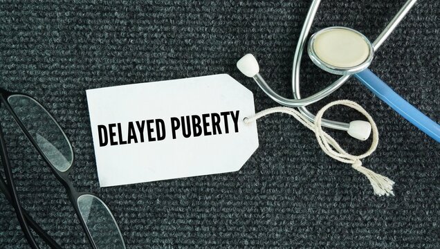 Stethoscope and paper tag with the words Delayed puberty is defined as the absence of physical signs of sexual maturation by age 13 in girls -no breast development or age 14 in boys -no testicular enl