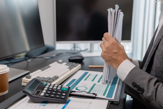 Business professional reviewing financial reports and using a calculator at a modern office desk, analyzing budget data, accounting documents, and business performance for financial planning.