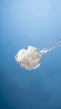 Sweet Sugar Cubes in Transparent Spoon on Blue Background