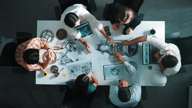 Top view of smart engineer team in casual cloth talking about turbine engine structure at table with metal gear, calculator, sticky notes. Group of technician taking a note in meeting. Alimentation.