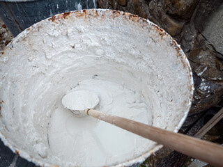 Traditional wooden ladle in a bucket of slaked lime at a construction site. Close-up of lime mortar preparation for masonry, plastering and historic building restoration. © Marek