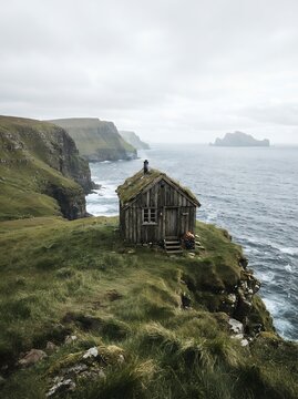 Rustic wooden cabin perched on a grassy cliff overlooking the ocean.