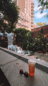 Iced tea and sunglasses on a stone ledge overlooking a city waterfall