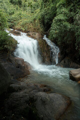 A serene waterfall cascades over rocky terrain, surrounded by lush green foliage. © k33pcalmncapture