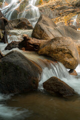A serene waterfall cascading over large, moss-covered rocks into a calm pool of water below. © k33pcalmncapture