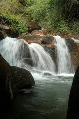 A serene waterfall cascades over smooth rocks into a tranquil pool, surrounded by lush greenery. © k33pcalmncapture
