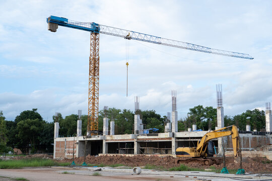 Tall tower crane standing at dynamic construction site with concrete building structure and yellow excavator under blue sky showing ambitious development progress