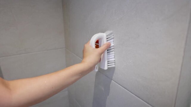 Woman Scrubbing Bathroom Wall Tiles with a White Bristle Brush
